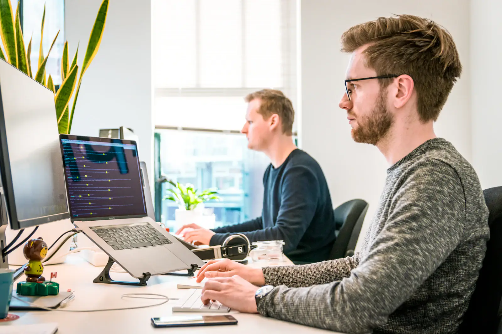 Two engineers working side by side at computers in a bright office.