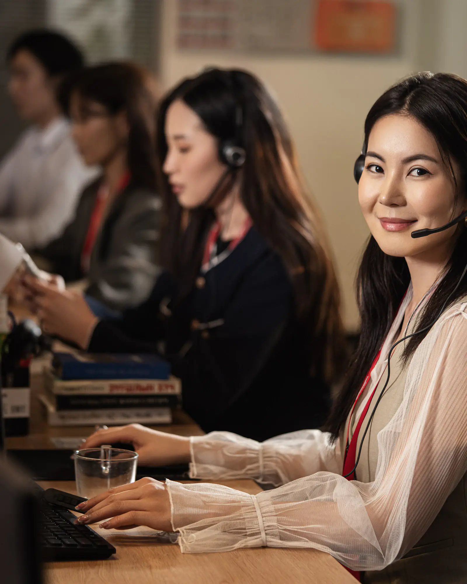 A service desk analyst wearing a headset, working at a computer with colleagues behind her.